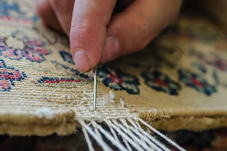 Retissage à l'aiguille du bord d'un tapis d'Orient à la main, geste artisanal de précision